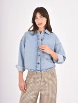Sobrecamisa de denim en tono azul claro, con corte oversize, cuello clásico, cierre frontal con botones metálicos y un bolsillo de parche en el pecho.