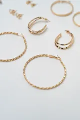 Set de siete pares de aros dorados de diversos estilos, incluyendo aros de argolla lisos, argollas texturadas, aros ovalados y aros pequeños tipo broche con diferentes formas.