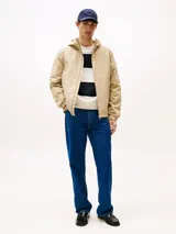 Campera beige de nailon repelente al agua y resistente al viento, con capucha fija, cierre de cremallera, dos bolsillos en la cintura, bolsillo interior con cremallera, puños elásticos con botones a presión, solapa de protección en la parte trasera y parche con el logo de Tommy Hilfiger en la manga.