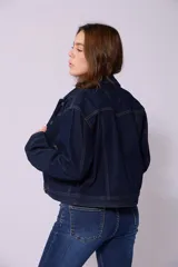 Campera de jean de mujer, color azul claro lavado, con corte cropped y estilo clásico. Presenta cuello camisero, botones metálicos frontales y bolsillos de parche en el pecho.