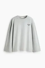 Top oversized de punto de algodón suave en color gris melange, con diseño estampado de letras pequeñas en el pecho. Presenta manga larga, cuello redondo ribeteado y hombros caídos.