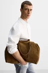 Bolso de mano marrón de cuero con acabado serraje. Tiene un compartimento principal con cierre de cremallera, dos bolsillos interiores (uno con cremallera) y asas de mano de cuero.