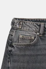 Jeans de tiro medio con diseño wide leg y cinco bolsillos. Presenta costuras verticales marcadas en el delantero y cierre frontal con cremallera y botón.