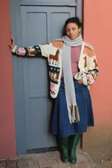 Cardigan tejido a mano en lana merino, con diseño multicolor de inspiración andina que incluye motivos de llamas, franjas geométricas y detalles en tonos beige, marrón, negro y rosa.