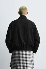 Cazadora de hombre color verde oliva, estilo bomber o Harrington, con cuello subido, cierre frontal de cremallera y puños y bajo elásticos. Presenta bolsillos de plastrón con solapa en el pecho y bolsillos de vivo en la cadera.