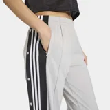Pantalón deportivo Adidas Adibreak de color gris, con franjas negras laterales y las clásicas tres tiras blancas. Cuenta con botones a presión en los laterales, cintura elástica y diseño holgado.