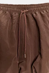 Falda pantalón de tiro medio con diseño tipo globo, confeccionada en tejido satinado color marrón. Presenta cintura elástica con cordones trenzados ajustables.