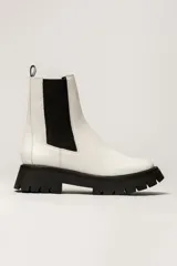 Bota corta estilo Chelsea de cuero blanco, con elástico lateral negro y suela track gruesa negra.