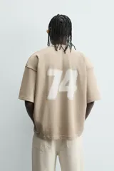 Sudadera de corte relajado, color beige claro, con cuello redondo y manga corta. Presenta un estampado frontal con texto en blanco difuminado que dice "SCREEN PLAYER" y debajo "Hypercore Technology".