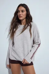 Sweater de tejido de punto con calce relajado, cuello redondo y mangas largas. Presenta un diseño de rayas verticales en contraste a lo largo de las mangas, aportando un estilo deportivo.