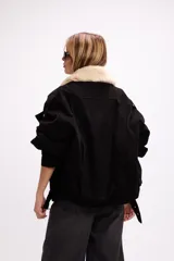 Campera de gamuza color marrón con cuello de corderito sintético en color crema. Presenta un diseño oversize con cierre frontal, solapas con broches metálicos y una tira ajustable en el ruedo.