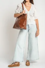 Bolso tipo shopper color marrón de cuero sintético con diseño trenzado. Cuenta con doble asa de hombro y placa metálica con el logo de la marca en el frente.