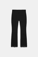 Pantalón negro de tiro alto con cintura elástica, confeccionado en tejido elástico. El bajo es acampanado (mini flare) y está decorado con encaje a tono.