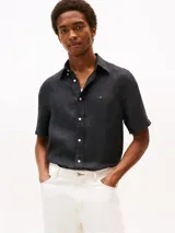 Camisa de lino de corte regular, color negro con efecto pigmentado y ligeramente desgastado. Presenta cuello clásico, cierre frontal con botones blancos y logo de Tommy Hilfiger bordado en el pecho.