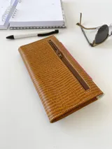 Billetera de cuero con diseño tricolor que combina texturas: cuerpo principal en marrón con textura tipo lagarto, solapa central en fucsia con textura granulada y detalles en blanco con textura tipo cocodrilo. Incluye una etiqueta central de cuero en color tostado con la marca grabada y cierre con broche.
