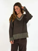 Sweater de tejido acanalado en color marrón oscuro, con cuello en V y detalles en tono metalizado en el cuello, puños y ruedo. Presenta un corte holgado y mangas largas.