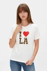 Remera blanca de manga corta y cuello redondo, con corte holgado y estampado frontal que dice 'I <3 LA' con letras de animal print y un corazón rojo.