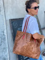 Bolso tote de cuero color marrón con asas trenzadas en marrón y rojo.