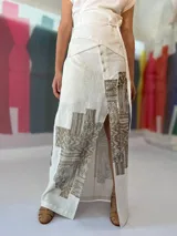Falda larga blanca de lino y algodón con estampa exclusiva en cobre laminado. Corte asimétrico, tajo central y un bolsillo lateral. Cierre frontal con broches a presión.
