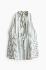 Top halter color beige y azul a rayas, con escote en V pronunciado, tirantes anchos para atar al cuello y detalle de moño ajustable en el centro del pecho. Diseño holgado con leve vuelo en el bajo.
