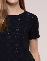 Remera blanca de calce recto con diseño de bordado calado estilo broderie, cuello redondo clásico y mangas cortas.