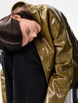 Campera corta de estilo moderno con acabado engomado brillante, cuello camisero, cierre frontal con botones a presión ocultos y bolsillos laterales.