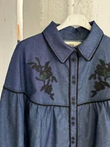 Camisa negra de manga larga con canesú estampado con diseño floral, cuello camisero y cierre frontal con botones.