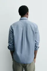 Camisa de corte relajado confeccionada en una mezcla de lyocell y algodón con efecto lavado. Presenta cuello solapa, manga larga con puños abotonados, bolsillo de plastrón en el pecho y cierre frontal con botones.