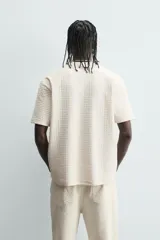 Camiseta de manga corta color crema, con cuello redondo y tejido texturizado con estructura.