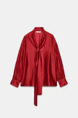 Camisa de lyocell satinado color rojo, con cuello alto, escote en V y largas tiras para anudar al cuello. Tiene mangas largas amplias con puños anchos y diseño holgado.