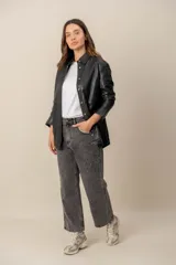 Campera estilo sobrecamisa confeccionada en cuero negro, de corte recto, con cuello camisero y cierre frontal de botones metálicos a presión.