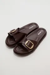 Sandalia plana de eco cuero negro, con tira ancha en el empeine decorada con una hebilla metálica dorada cuadrada y suela dentada.