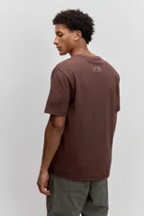 Remera de algodón color marrón chocolate, de corte clásico y cuello redondo, con un pequeño estampado gráfico en el pecho.