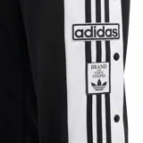 Pantalon deportivo Adidas modelo Adibreak, color negro con franjas laterales blancas y botones a presion a lo largo de las piernas. Presenta el logo de la marca y el emblema de la coleccion en el lateral.