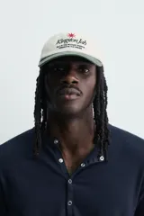 Gorra de seis paneles con efecto lavado, de color blanco crudo con visera en verde militar. Presenta un bordado frontal contrastante con texto en negro y una estrella roja.