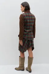 Chaqueta de lana en tono verde oliva con textura jaspeada, cuello mao y detalle de volado frontal. Presenta un corte entallado, bolsillos delanteros con solapa y cierre frontal con botones.