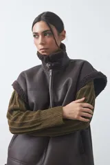 Chaleco de cuero sintético negro con interior y detalles de corderito en cuello, sisas y ruedo. Presenta cierre frontal completo y diseño holgado.