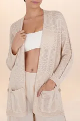Cardigan largo color beige de tejido de punto ligero, con diseño abierto y holgado, mangas largas, bolsillos frontales y botones decorativos en los costados.