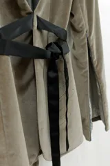 Blazer tipo smoking de terciopelo negro con acabado brillante y detalles estampados en dorado. Presenta solapas clásicas, cierre frontal cruzado mediante un lazo y mangas largas con cierres incorporados. El diseño es entallado y sofisticado.