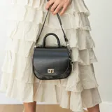 Cartera negra con asa corta superior y correa larga desmontable. Tiene un cierre metálico dorado en la parte delantera y detalles en animal print en la parte inferior.