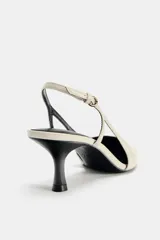 Zapato de tacón destalonado con tira trasera ajustable mediante hebilla metálica. Presenta un diseño de punta fina, escote redondo y tacón fino de altura media.