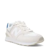 Championes urbanos New Balance modelo 574, color beige claro con detalles en blanco y azul metalizado en el talón. Confeccionados en una combinación de gamuza y malla, presentan el logo 'N' característico en los laterales y entresuela con tecnología de amortiguación.