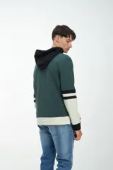 Canguro marrón con capucha forrada en verde oscuro, cordones de ajuste y bolsillo tipo canguro. Las mangas son largas, con puños verdes y franjas horizontales blancas y verdes.