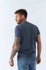 Remera de hombre color azul, con cuello redondo y manga corta. Presenta un diseño gráfico estampado en el frente con formas geométricas y letras en tonos blanco y gris.