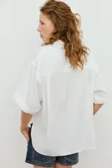 Camisa de manga corta y corte fluido, color marrón, con cuello solapa y cierre frontal con botones ocultos. Presenta bajo asimétrico con aberturas laterales y mangas con vuelta.