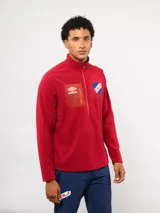 Buzo de micropolar rojo con medio cierre frontal, cuello alto y bolsillo en el pecho con cierre. Presenta el logo de Umbro y el escudo del Club Nacional de Football bordados en el frente.