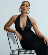 Vestido midi de color negro con escote halter y detalle metálico en el busto. Presenta fruncidos laterales que realzan la silueta y un diseño elegante y ajustado.