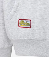 Buzo tipo hoodie con corte boxy, confeccionado en algodón con fondo melange. Presenta capucha, bolsillo canguro frontal, puños y ruedo acanalados, y múltiples parches bordados decorativos en el frente y las mangas.