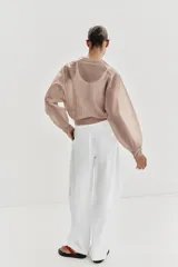 Chaqueta estilo bomber de punto color beige con acabado brillante, cuello redondo, manga larga con puños elásticos y cierre frontal con cremallera.