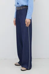 Pantalon de corte recto y pierna ancha, confeccionado en tela tipo denim color azul oscuro, con costuras a contratono y detalle de abertura lateral en el ruedo.